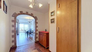 A hallway with a wooden door, a red countertop, and a dining area in the background.