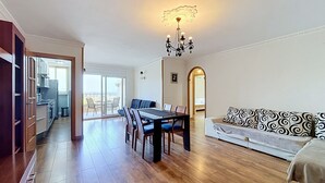 A spacious living area with a dining table, sofa, and a view to a balcony.