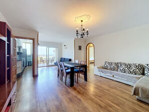 A spacious living area with a dining table, sofa, and a view to a balcony.