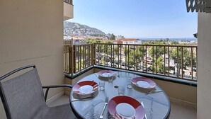 A balcony with a table set for four, overlooking a cityscape with buildings and a hill.