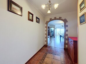 A hallway with a tiled floor, framed pictures on the wall, and a wooden cabinet with a red top. - SANT JOAN 3 4 Roses / Roses - INTERimmo (Rosas / Roses)
