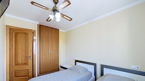 A bedroom with two beds, a wooden wardrobe, and a ceiling fan.