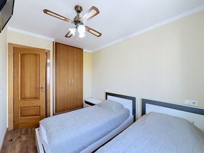 A bedroom with two beds, a wooden wardrobe, and a ceiling fan.