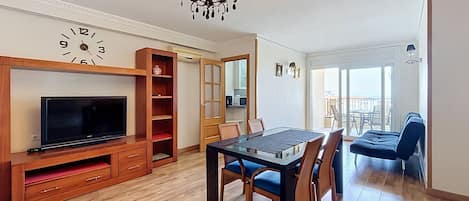 Un salon moderne doté d’un téléviseur à écran plat, d’un meuble de rangement en bois pour les appareils multimédias, d’une table à manger avec des chaises et d’un lustre.