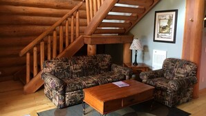 Interior d'una cabana de fusta amb unes escales de fusta, sofàs estampats, una taula de centre i una catifes.