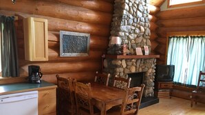 Interior acollidor d'una cabana amb una llar de pedra, taula de dinar de fusta i cadiretes.