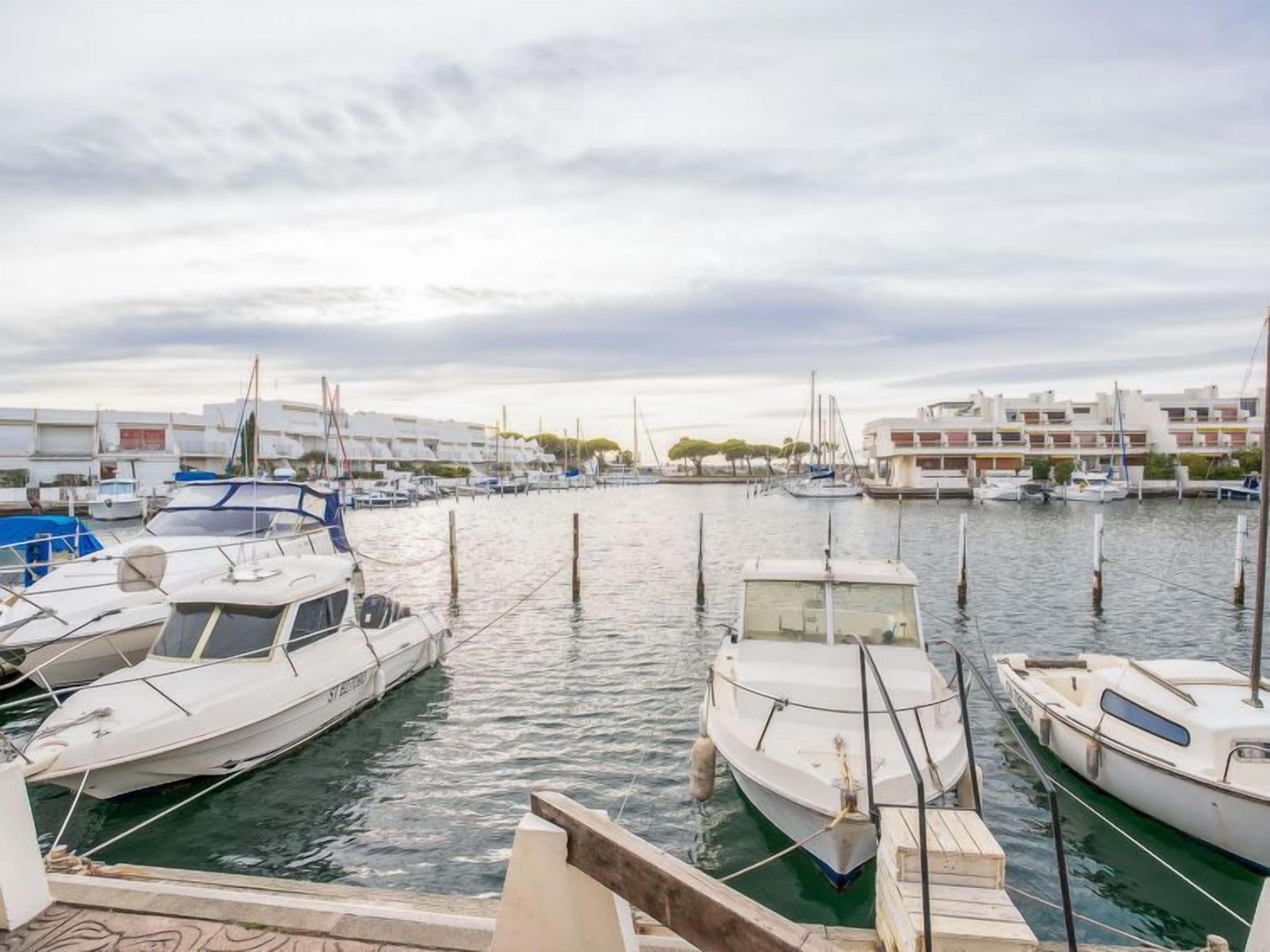 Un port de plaisance avec plusieurs bateaux amarrés, un ciel dégagé et des bâtiments en arrière-plan.