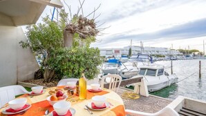 A dining table set with bowls, plates, and a bottle, overlooking a marina with boats.
