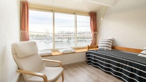 A room with a bed, a chair, and a view of a marina.