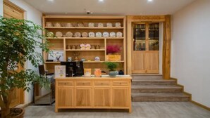 Zona de recepción con mostrador de madera, estanterías con diversos objetos, una máquina de café y una escalera que lleva a una puerta.