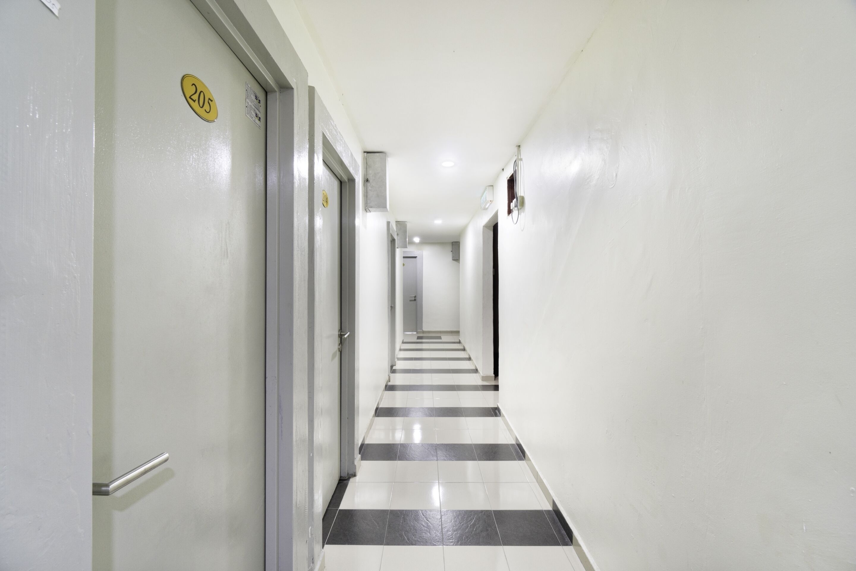 A corridor with a black and white tiled floor, white walls, and doors with numbers.