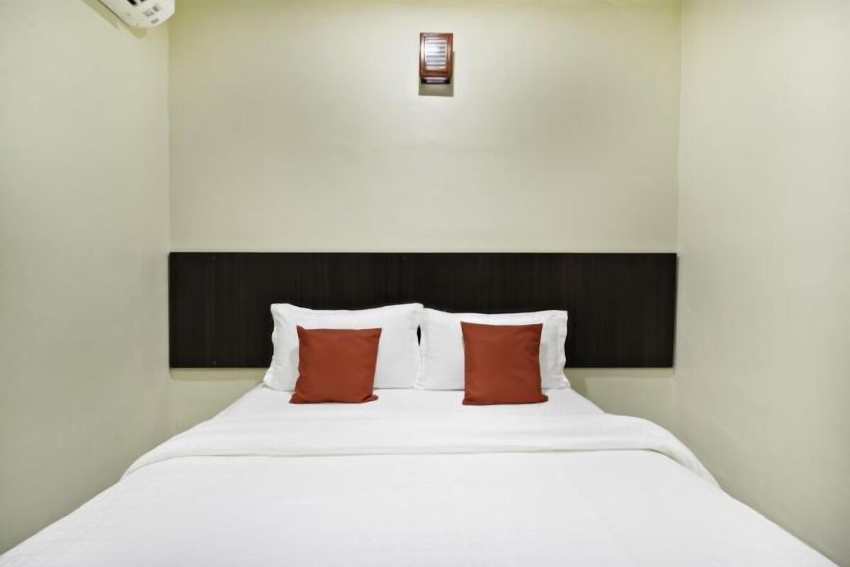A hotel room with a bed, two pillows, a headboard, and a wall-mounted light fixture.
