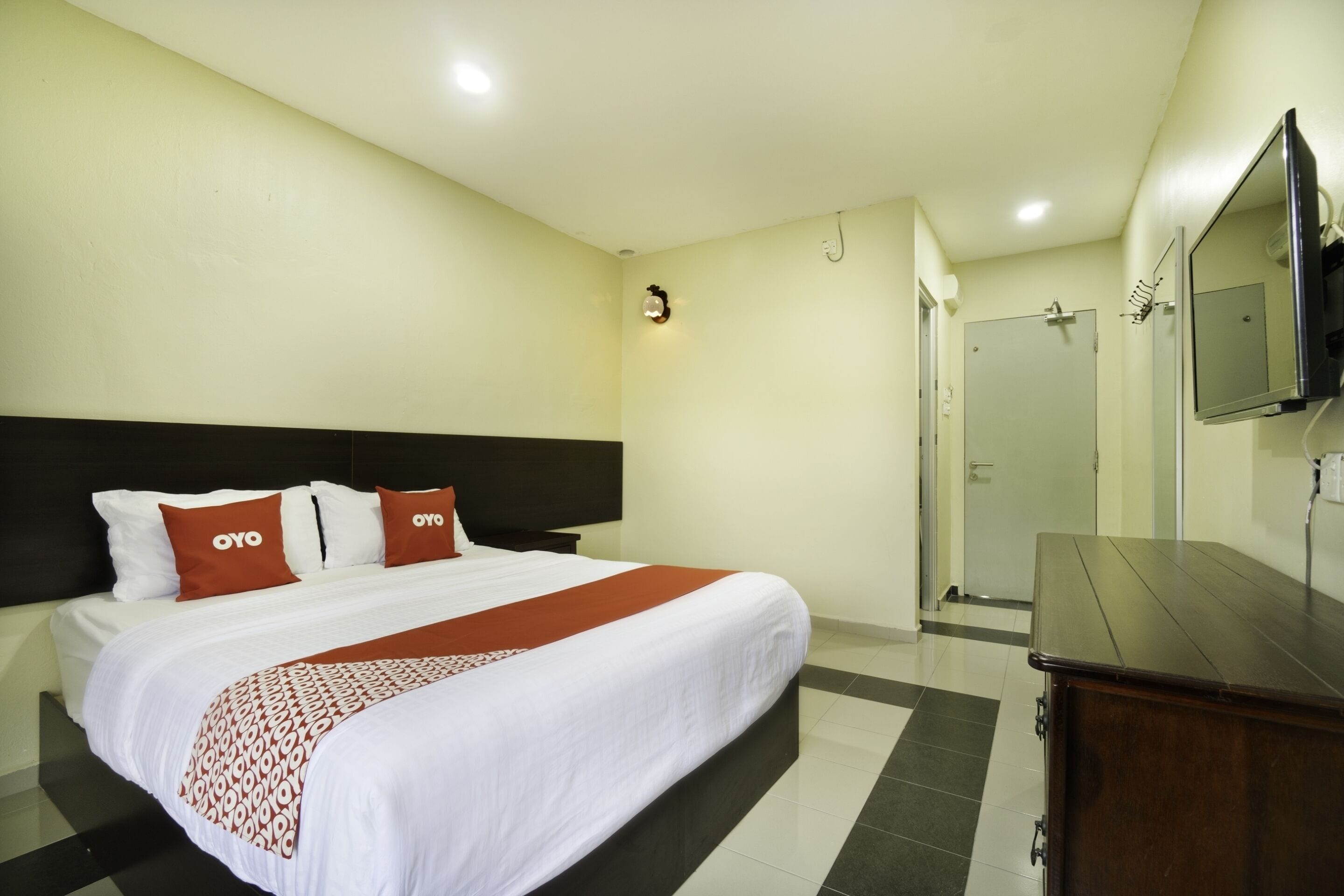 A hotel room with a large bed, a wooden dresser, a TV mounted on the wall, and a door leading to a bathroom.