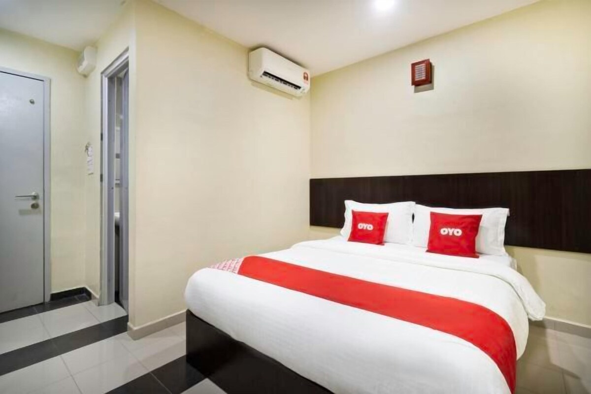 Una habitación de hotel con una cama, una puerta, un equipo de aire acondicionado y un detector de incendios instalado en la pared.