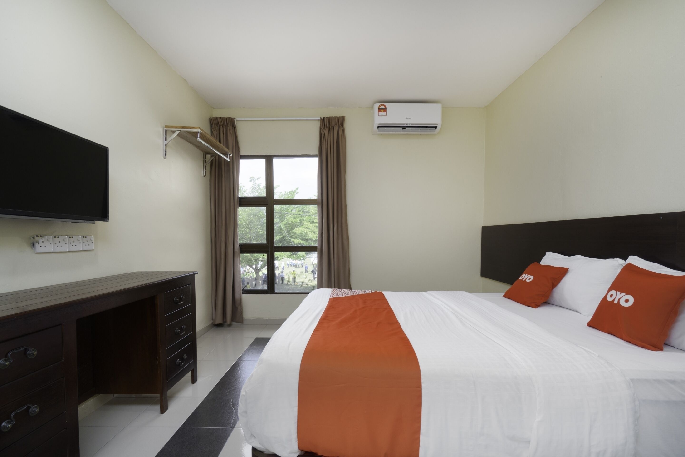 A hotel room with a bed, a desk, a TV, and an air conditioner.