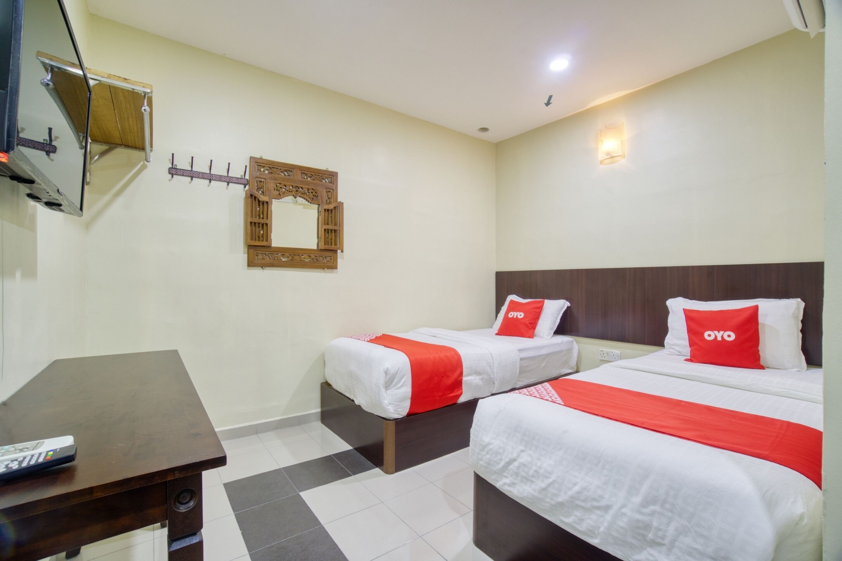 A hotel room with two beds, a wooden headboard, a small table with a remote control, and a wall-mounted mirror.