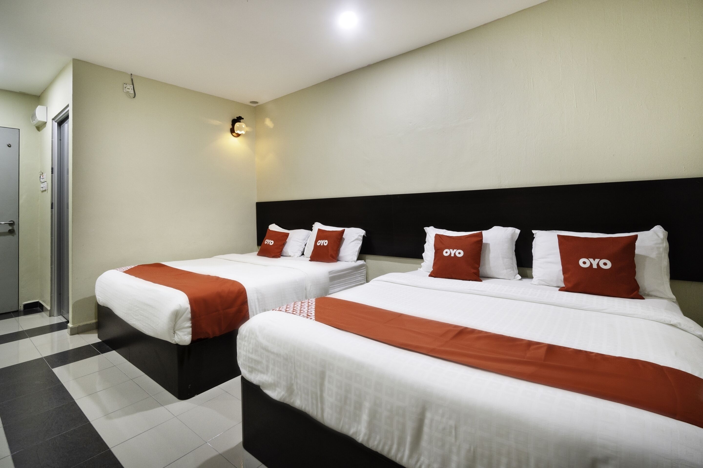 Two single beds with black headboards and white bedding, each with a red blanket and pillows labeled "OYO".