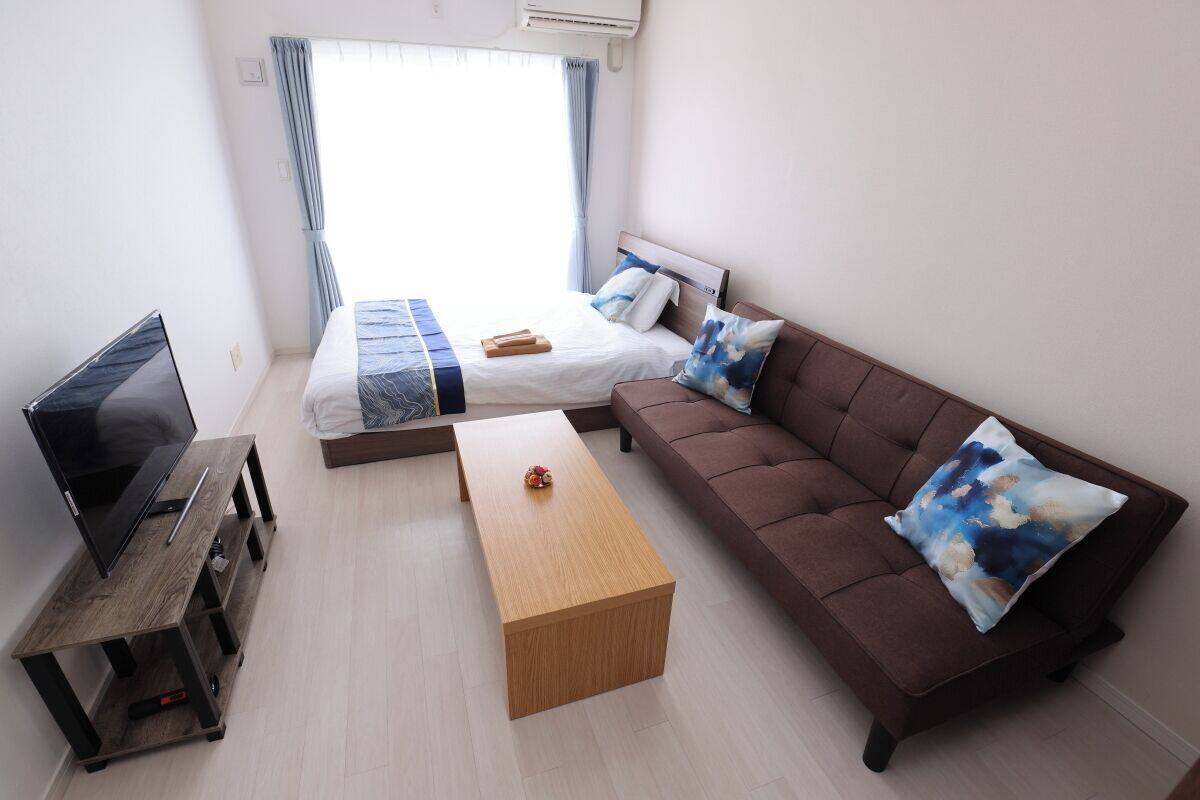 A modern living room with a sofa, a bed, a TV on a stand, and a wooden coffee table.