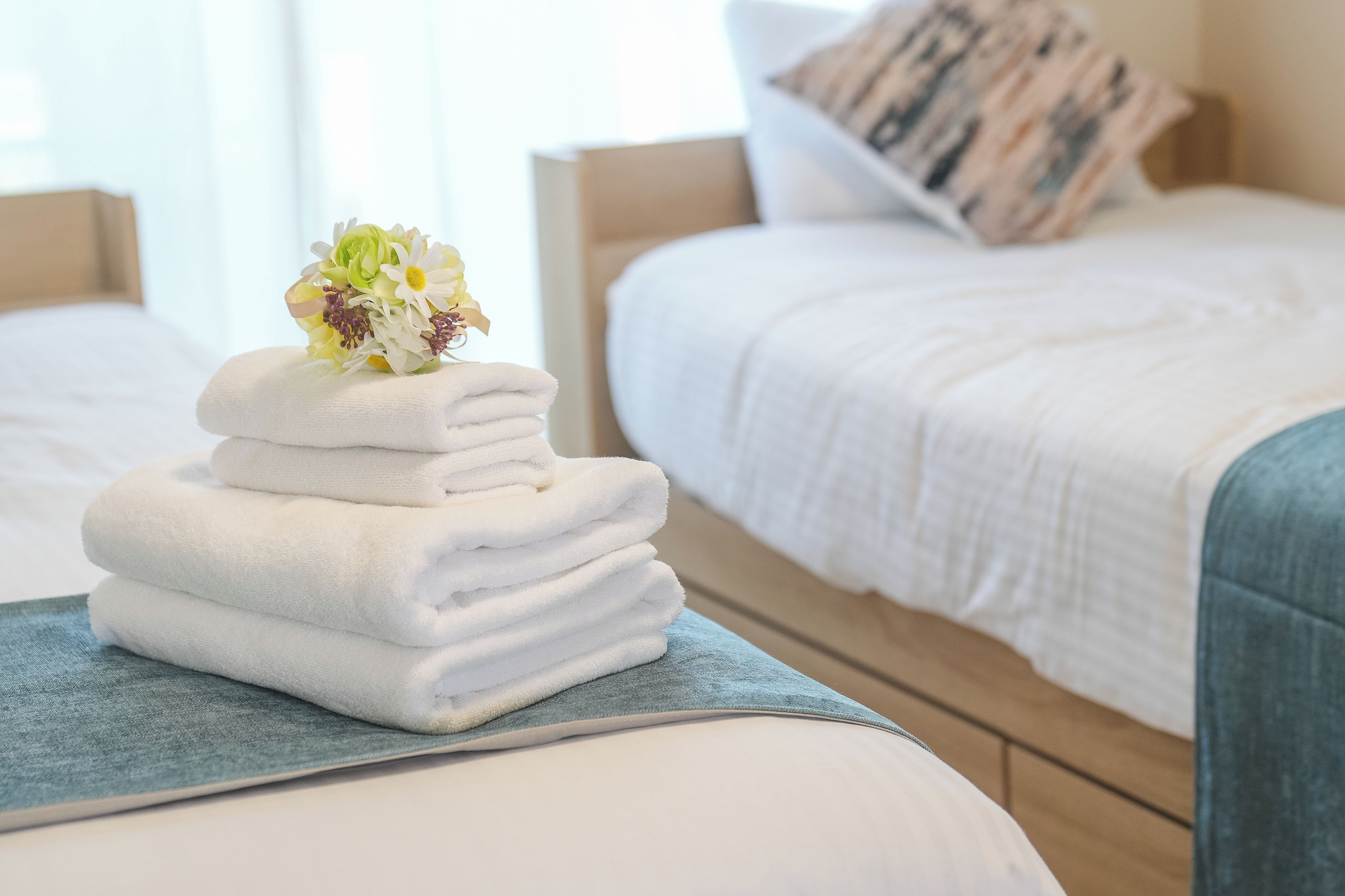 Ordentlich gefaltete weiße Handtücher auf einem blauen Handtuch auf einem Bett mit einem hölzernen Kopfteil und einem Kissen mit Streifenmuster.