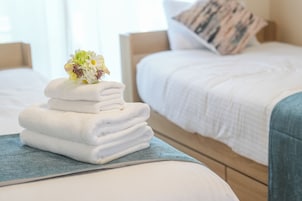 A neatly folded stack of white towels on a blue towel on a bed with a wooden headboard and a pillow with a striped pattern.