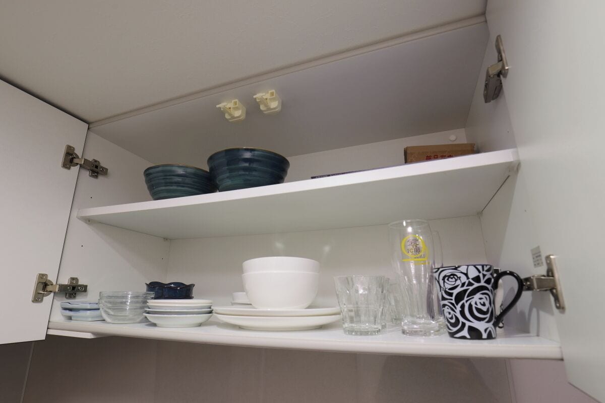 A kitchen cabinet with shelves holding various dishes, glasses, and a patterned mug.