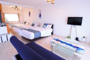 Una habitación de hotel moderna con dos camas, un televisor, una mesa de centro de vidrio y un sofá.