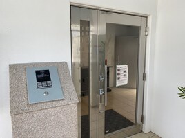 Entrada con puerta de vidrio y cerradura electrónica, un pequeño cartel en la pared y piso de baldosas.