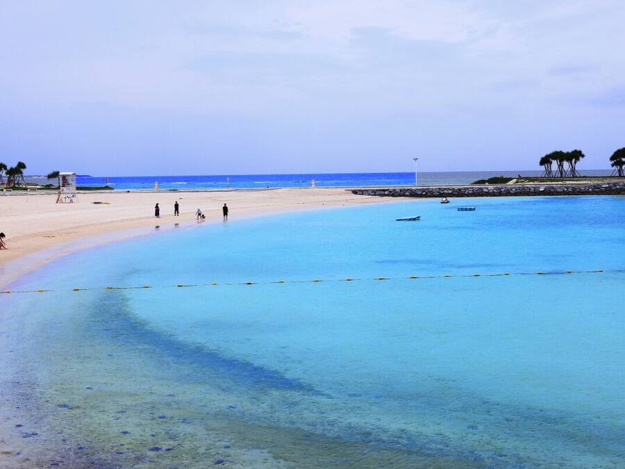 Una playa con aguas azules cristalinas, una orilla arenosa y algunas personas caminando.