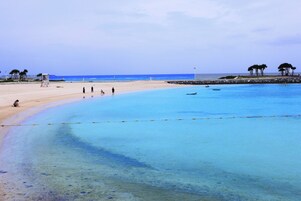 Una playa con aguas azules cristalinas, una orilla arenosa y algunas personas caminando.