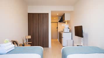 Una habitación de hotel con dos camas, un escritorio, una silla, un televisor y una kitchenette.