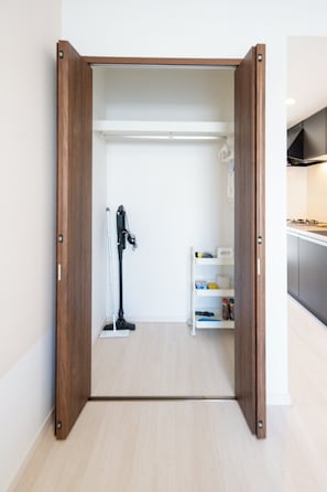 A walk-in closet with a wooden frame, a vacuum cleaner, and a white shelving unit. - Ocean View House Churaumi (Motobu)