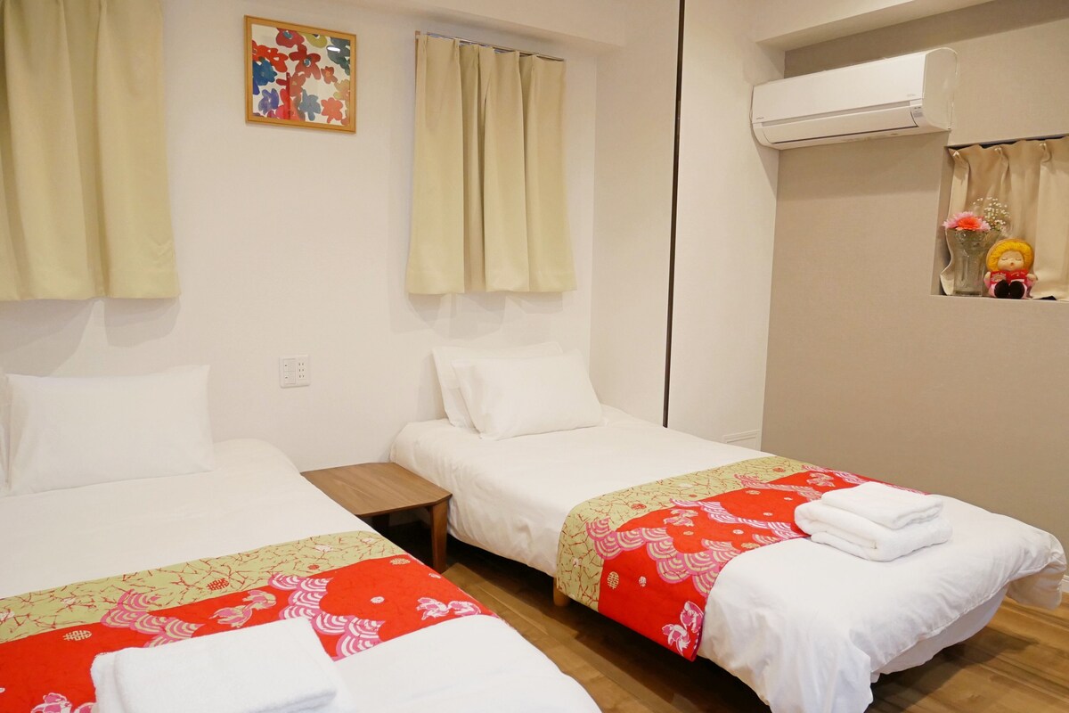 Ein Hotelzimmer mit zwei Betten, einem kleinen Tisch, einer Wandklimaanlage und einem dekorativen Gegenstand an der Wand.