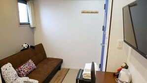 Ein kleines Zimmer mit einer Schlafcouch, einem kleinen Tisch, einem Fernseher und einem Fenster mit Vorhängen.