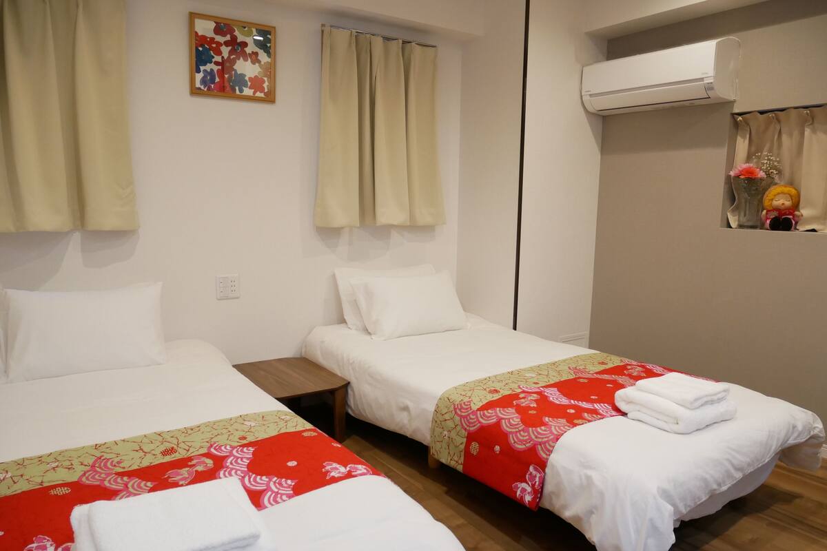 Une chambre d’hôtel avec deux lits simples, une petite table, un climatiseur fixé au mur et un objet décoratif sur le mur.