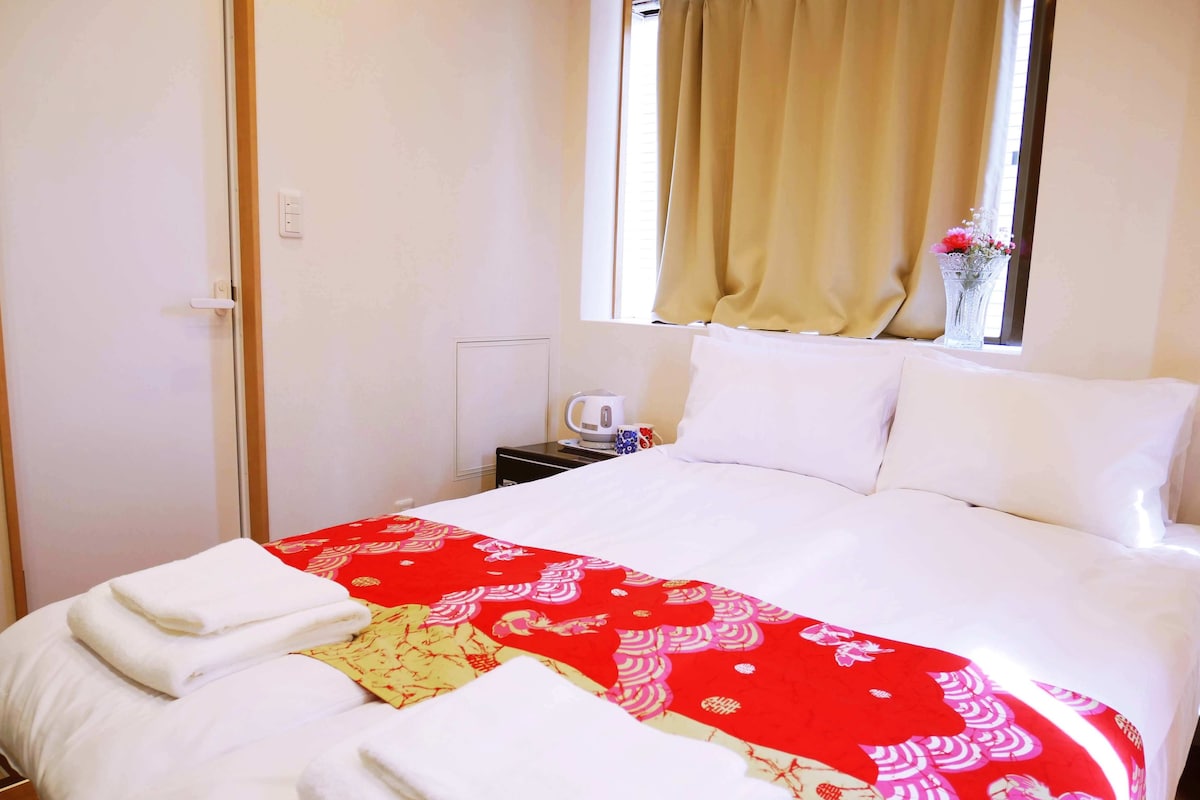 Ein Hotelzimmer mit einem Bett, einem Nachttisch mit Wasserkocher und einem Fenster mit Vorhängen.