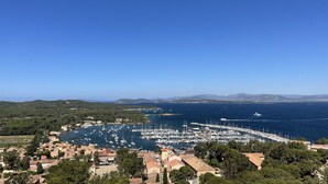 Une ville côtière dotée d’un port de plaisance rempli de bateaux, entourée de verdure et de bâtiments aux toits recouverts de tuiles rouges.