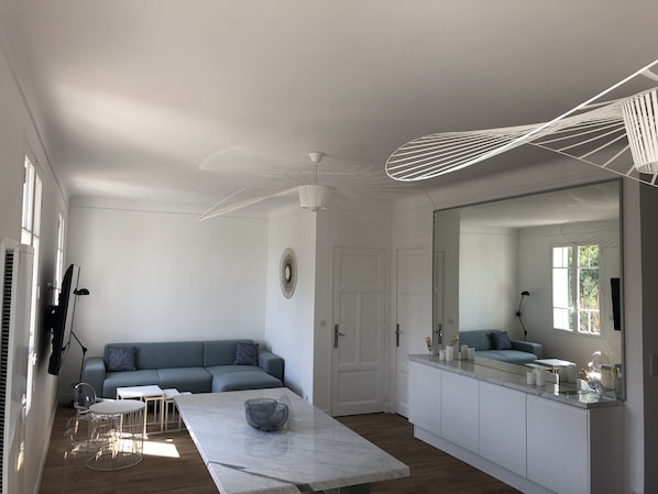 A modern living room with a sofa, a dining table, and a kitchen area with a large mirror and cabinets.