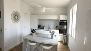 Une cuisine moderne dotée d’un plan de travail en marbre, de deux tabourets de bar, d’un four encastré et d’un luminaire au plafond au design original.
