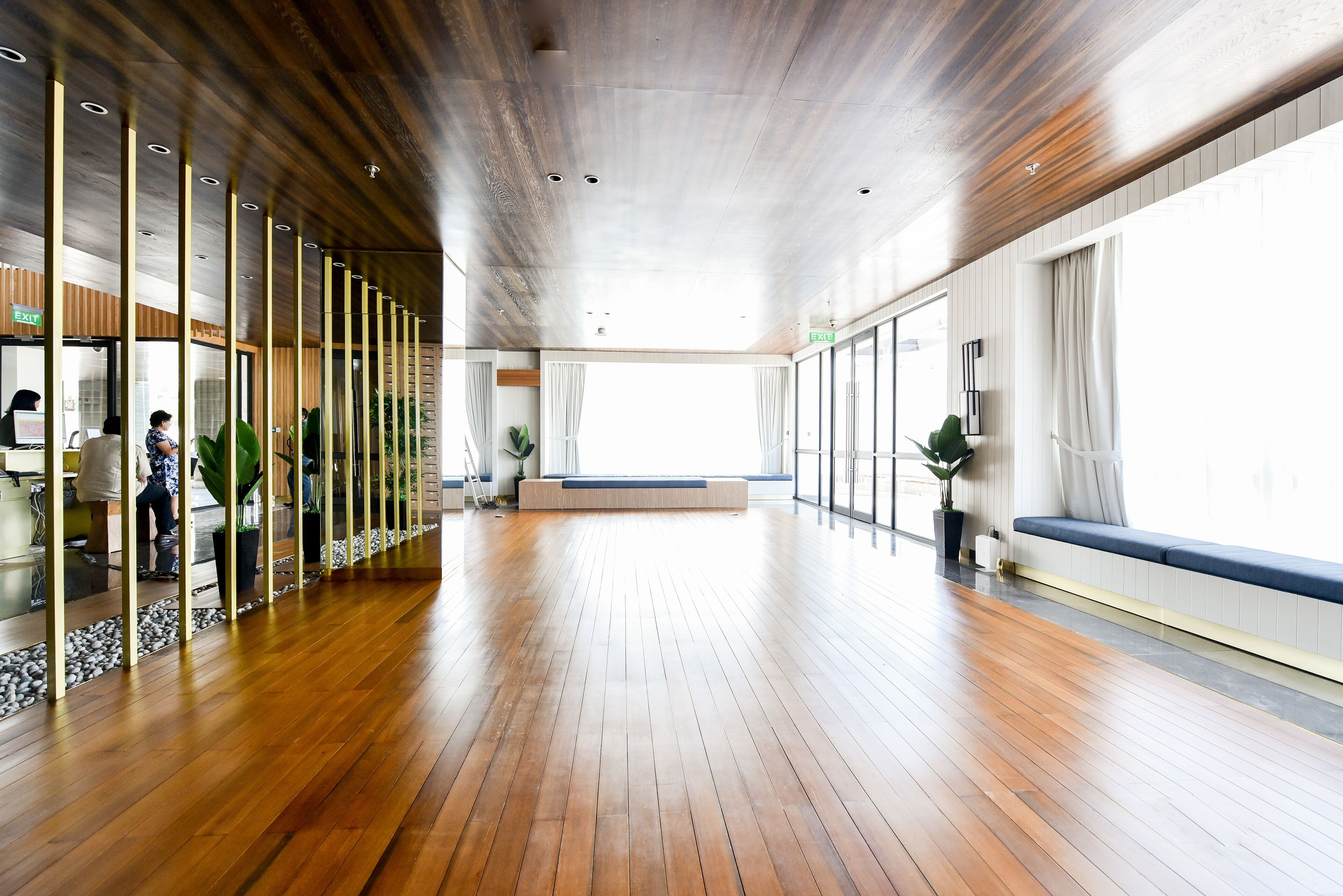 A spacious lobby with wooden flooring, glass partitions, and seating areas.