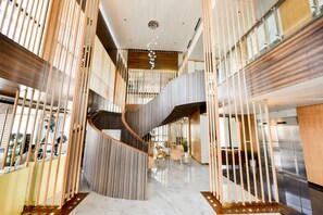 Un rebedor d'hotel modern amb una escala espiraltra central, terres de marbre polit i mobiliari contemporani.