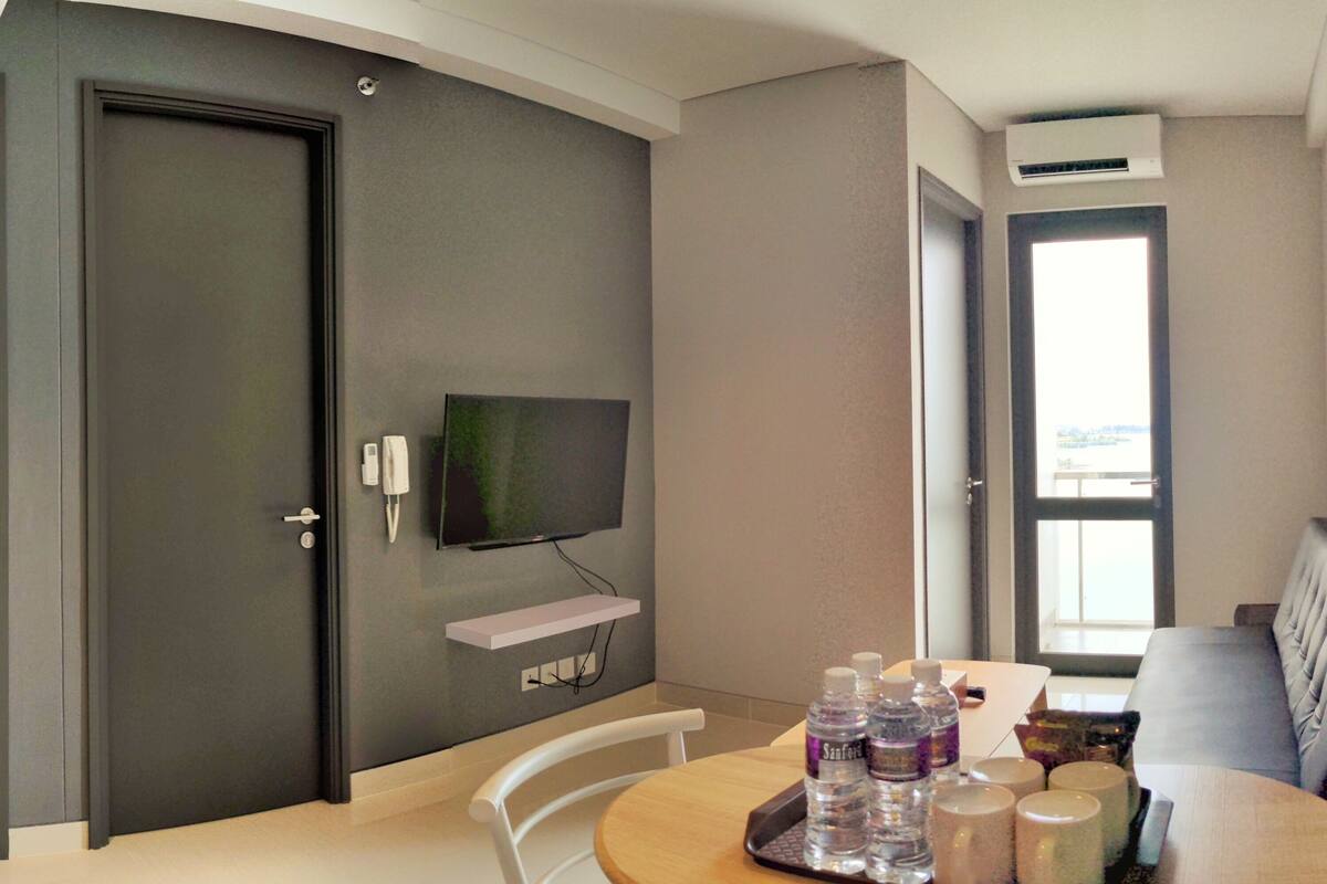 Ein Hotelzimmer mit an der Wand montiertem Fernseher, einem Esstisch mit Stühlen, einer Couch und einem Fenster mit Ausblick.