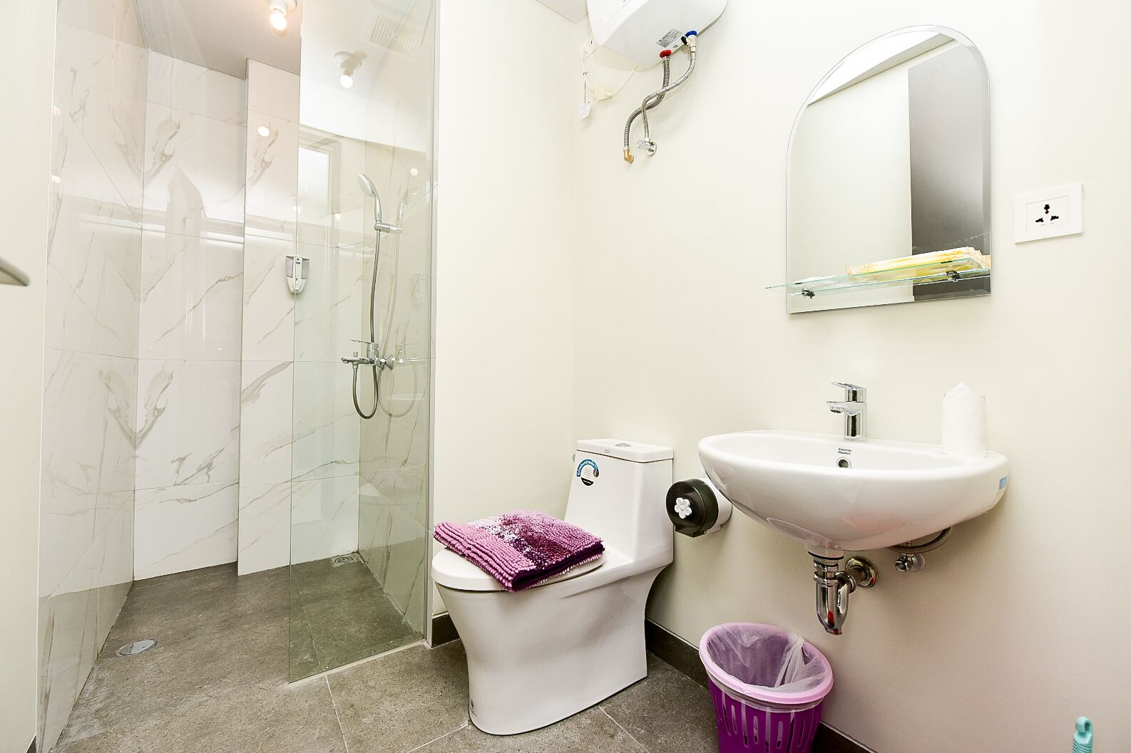 A bathroom with a glass-enclosed shower, a toilet, a sink, and a trash bin.