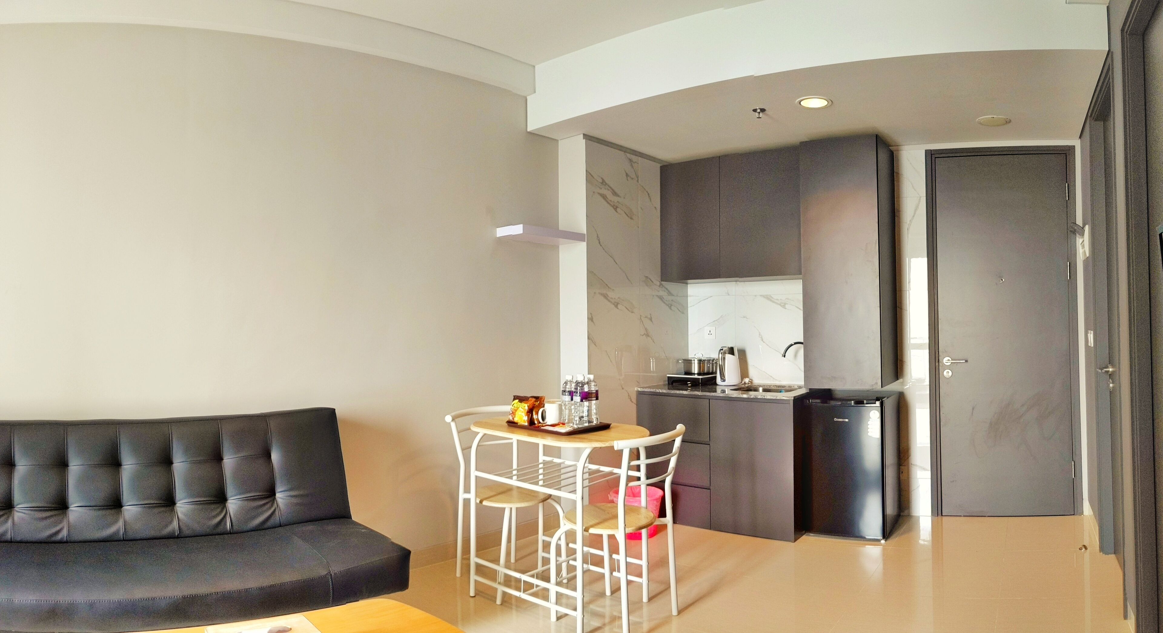 A compact living space with a sofa, a small dining table with chairs, a kitchenette, and a door.