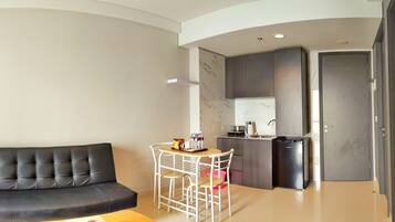 A compact living space with a sofa, a small dining table with chairs, a kitchenette, and a door.