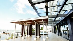 A spacious indoor area with a view of the sea, featuring a modern architectural design with glass walls and a wooden ceiling structure. -  Lovina at One Residence (Batam)