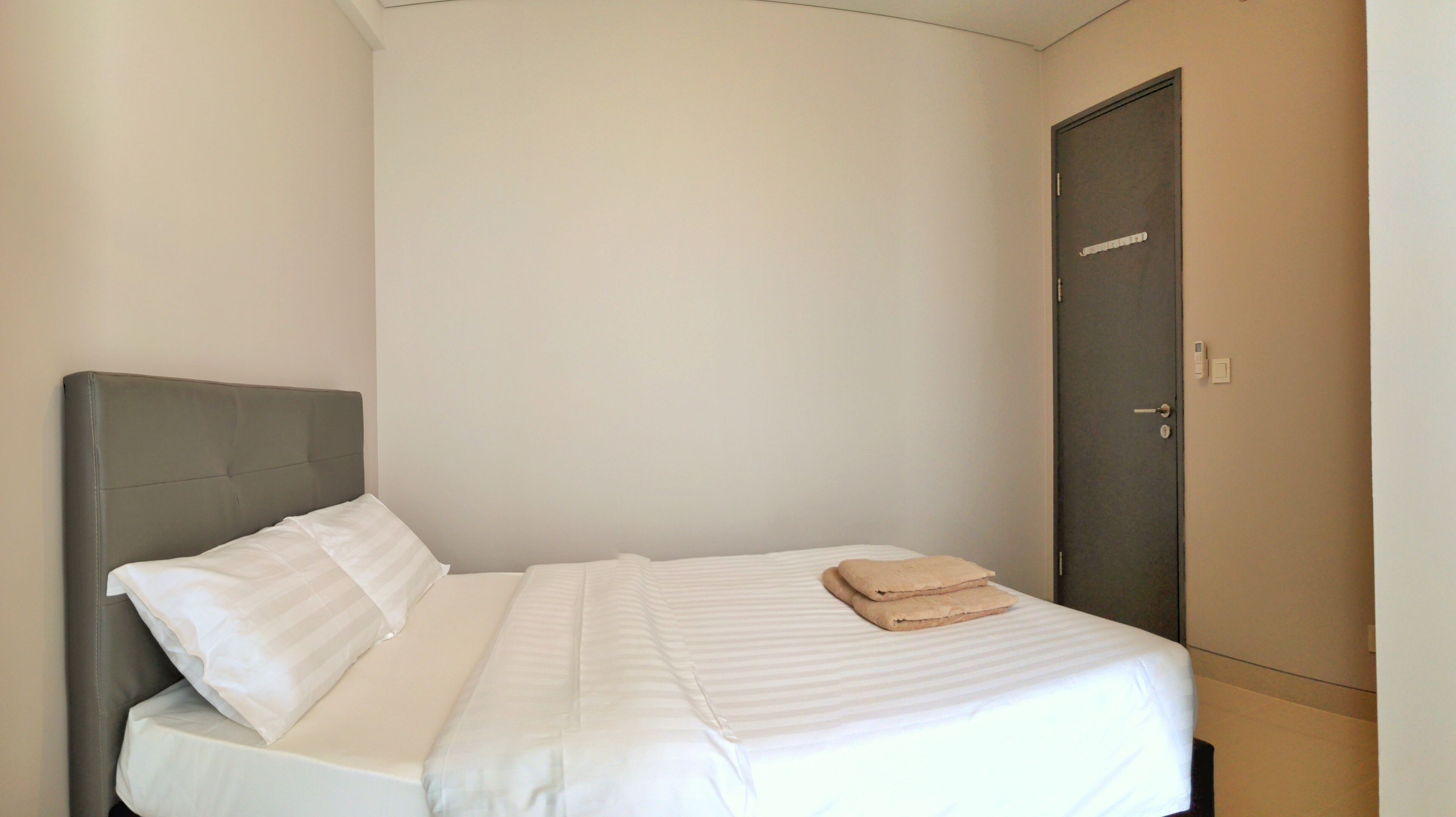 A single bed with a grey headboard and white bedding, a wooden nightstand, and a closed door.