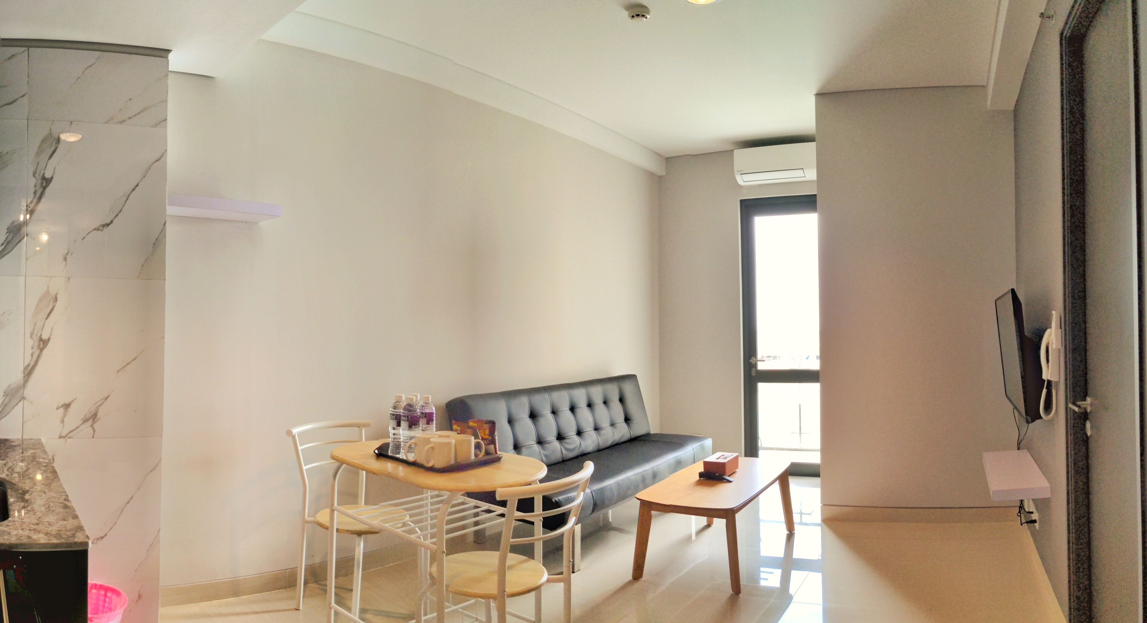 A modern living room with a marble-tiled wall, a black leather sofa, a wooden coffee table, and a white chair.