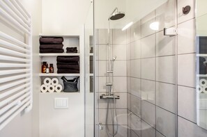 A modern bathroom with a glass-enclosed shower, white tiled walls, and shelves with towels and toiletries. - Matador Apartments Reykjavik (Reykjavik)