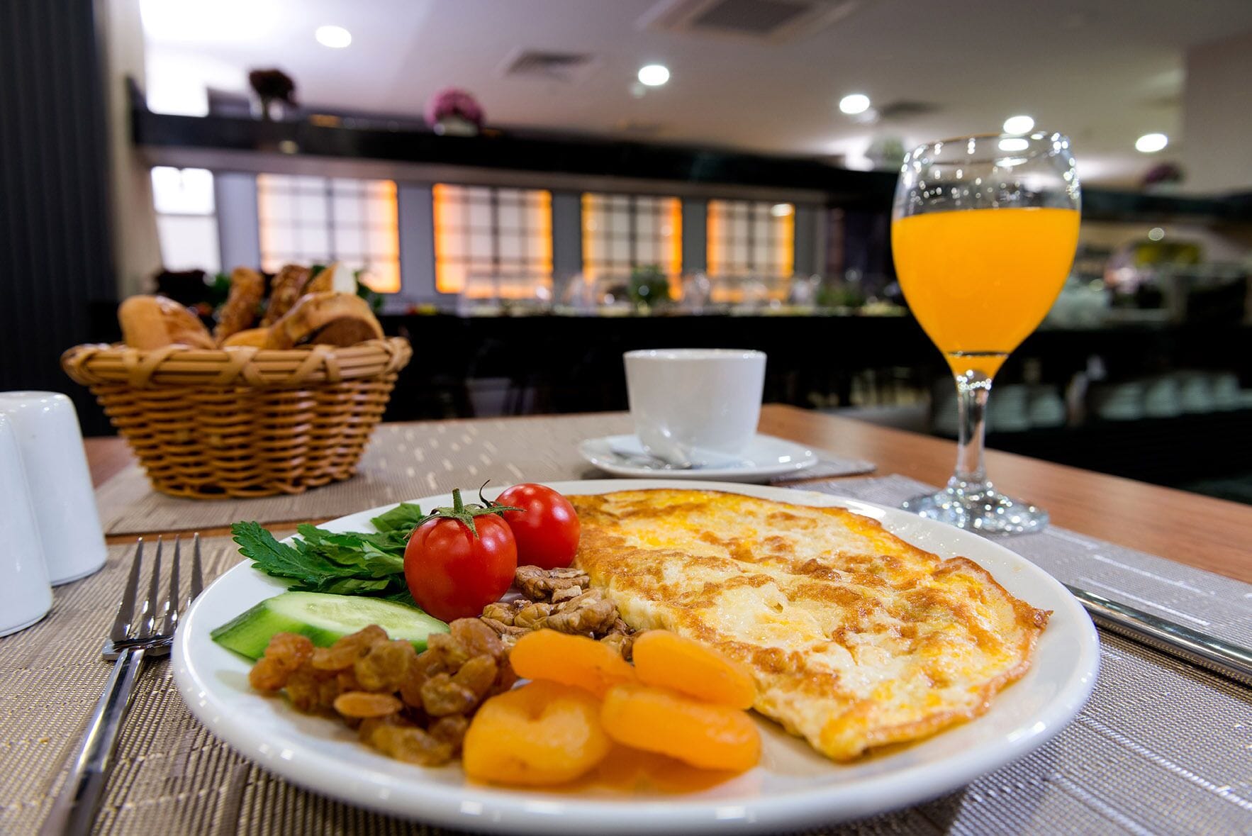 Un piatto per la colazione con uova, pomodori, cetrioli e carote, un bicchiere di succo d'arancia e un cestino di pane su un tavolo in un ristorante.