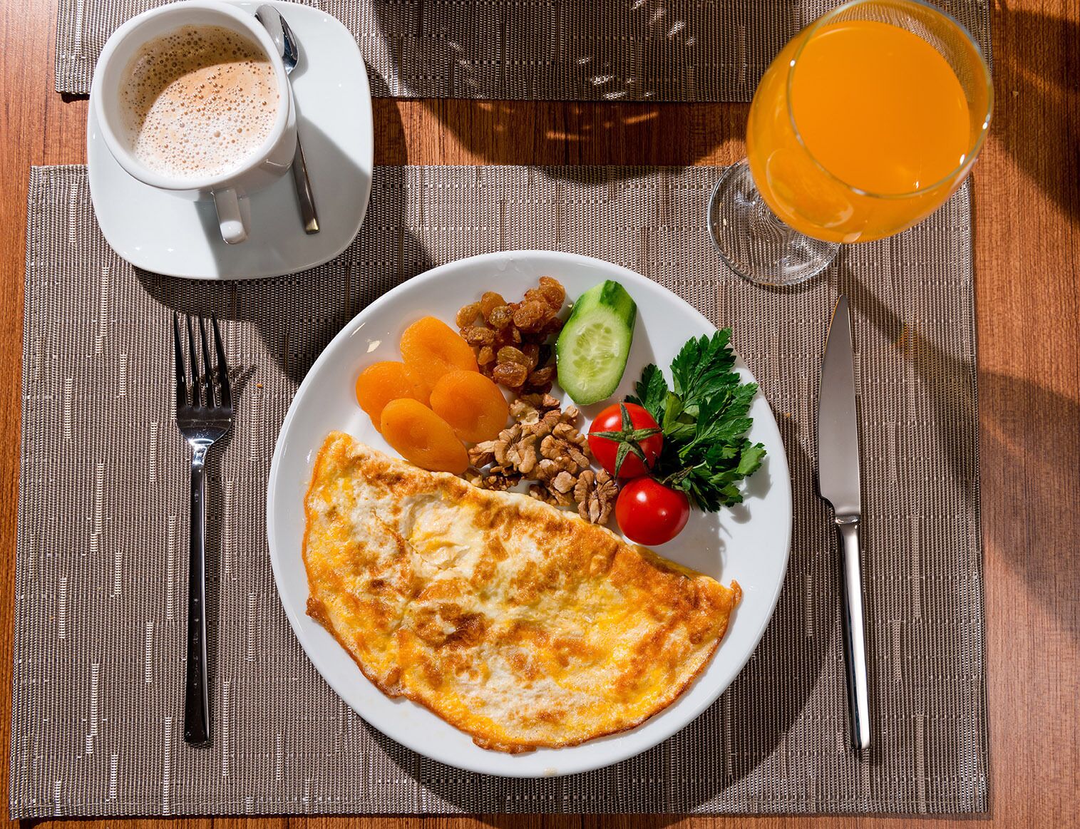 Une assiette de petit-déjeuner avec une omelette, des fruits et des légumes, une tasse de café et un verre de jus d’orange, le tout posé sur une table.